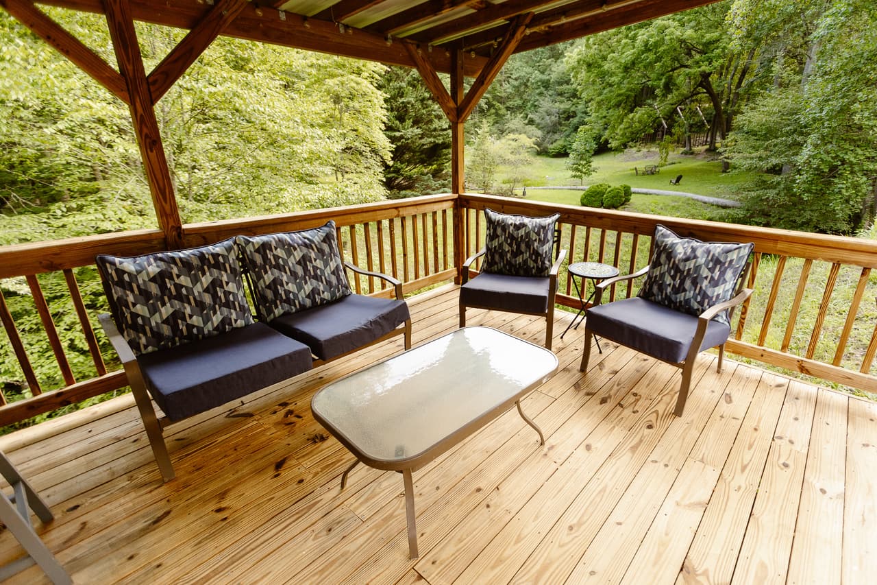 A covered deck with cushioned seating looking out over the lawn and the woods